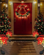 Solar poinsettia stake lights either side of a front door at night; sold singly, trees and wreath not included