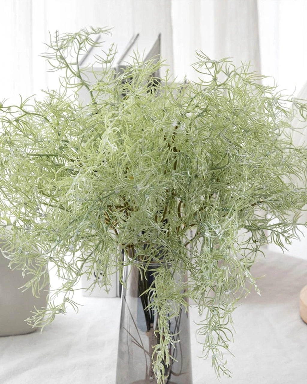 Artificial rosemary sprays in a silver vase on a white table; vase not included