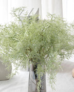 Artificial rosemary sprays in a silver vase on a white table; vase not included