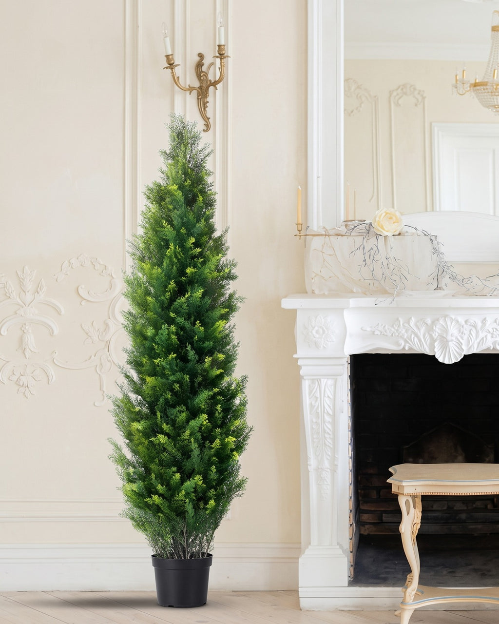 One of the cedar topiary trees in its black nursery pot beside a white carved fireplace