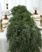 An artificial cedar garland laid along a dining table between candlesticks