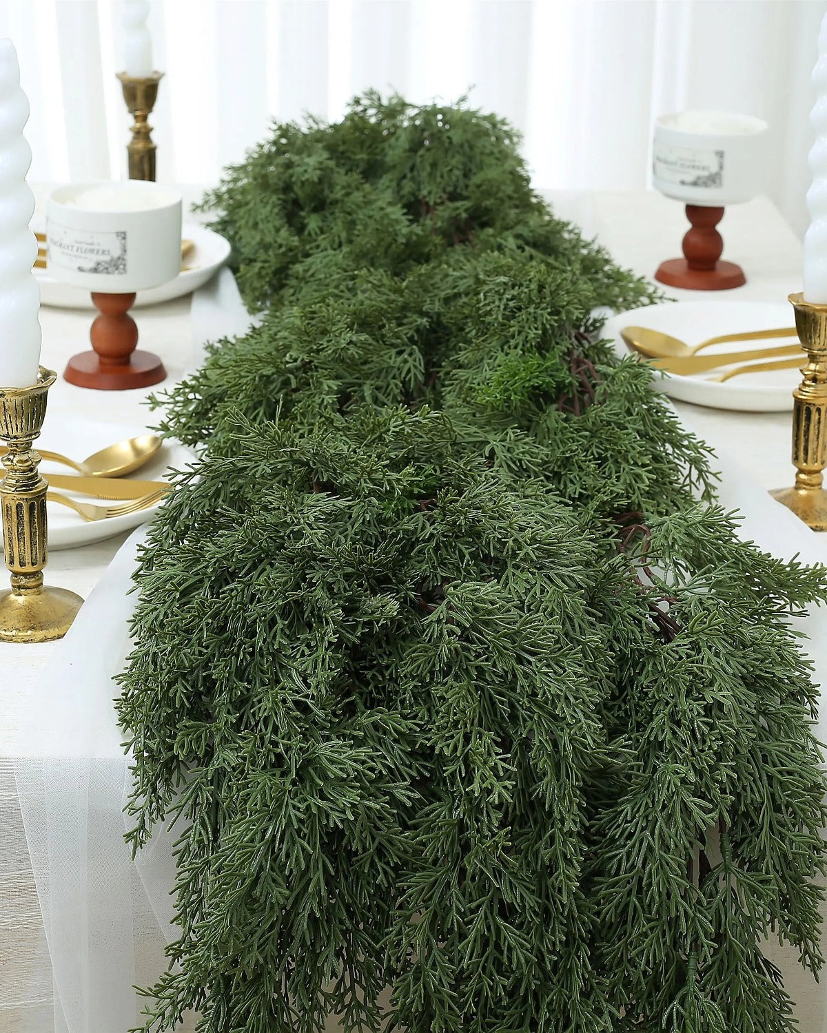 An artificial cedar garland laid along a dining table between candlesticks