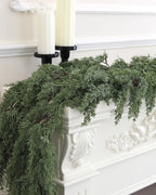 An artificial cedar garland trailing over a white carved mantel under two candles