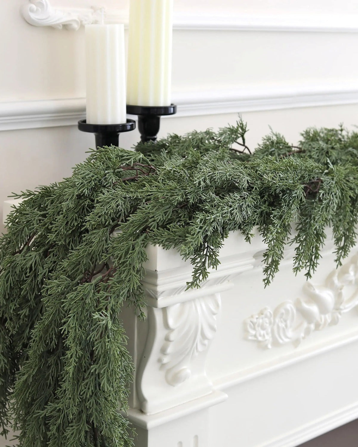 An artificial cedar garland trailing over a white carved mantel under two candles