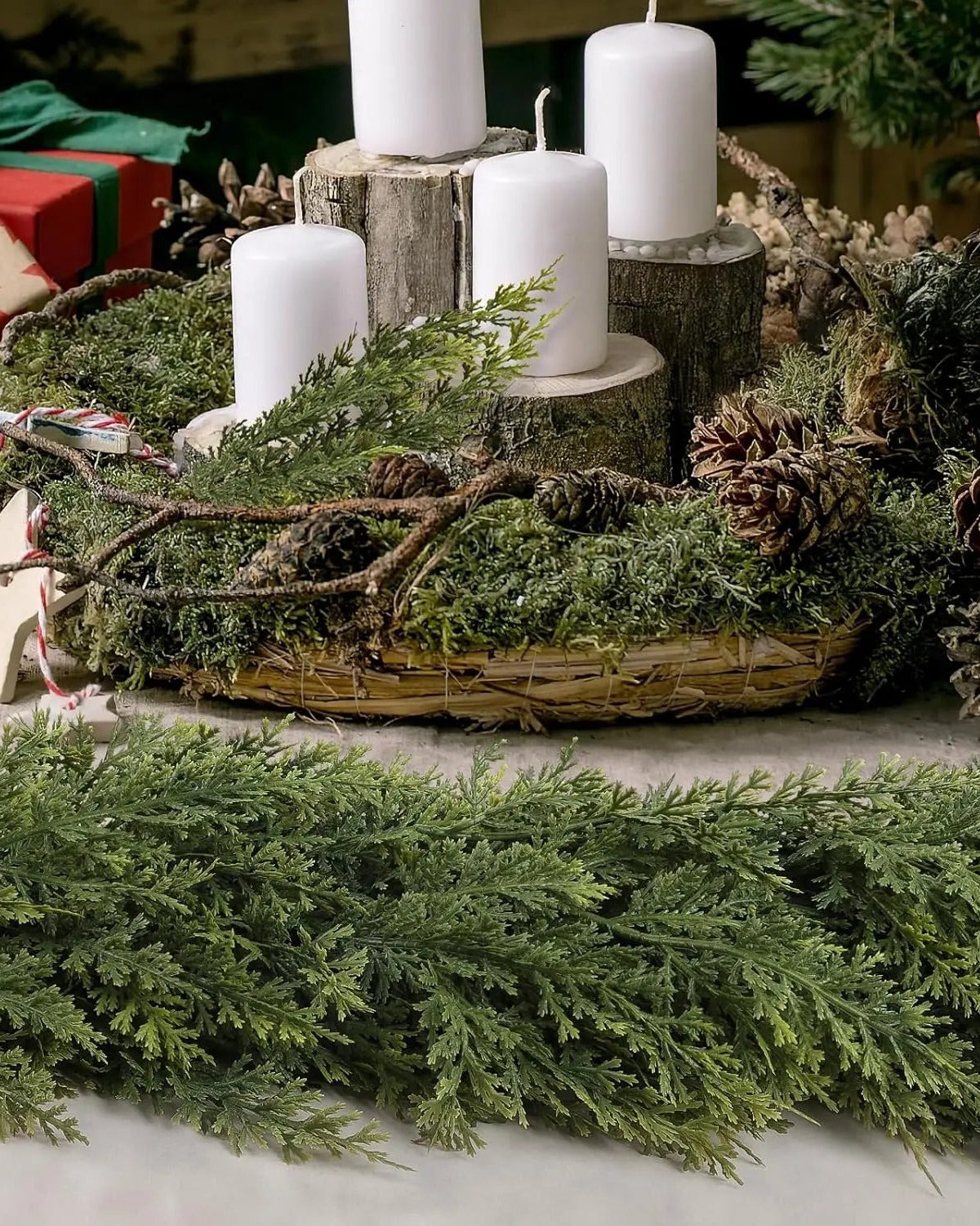 An artificial cypress garland in front of a candle centerpiece; candles, basket and pinecones not included