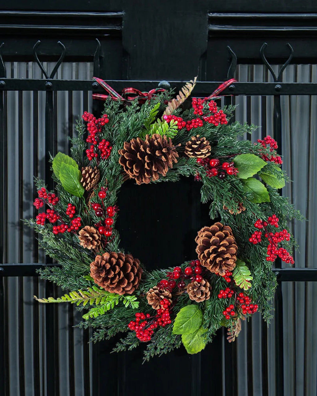 The cypress and pinecone wreath hung on a black gate; the plaid ribbon is not included