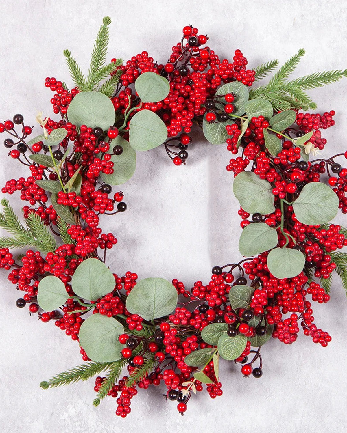 The berry and eucalyptus wreath on a pale stone ground, red berries, eucalyptus leaves and pine sprigs