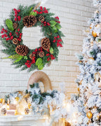 The cypress and pinecone wreath on a white brick wall beside a flocked tree; tree and mantel decorations not included