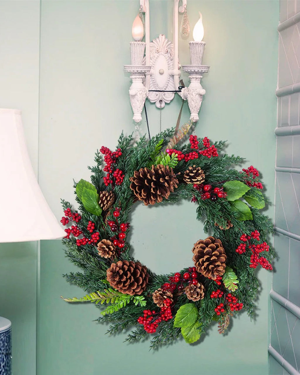 The cypress and pinecone wreath hung below a wall sconce beside a lamp