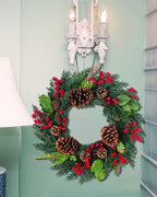 The cypress and pinecone wreath hung below a wall sconce beside a lamp