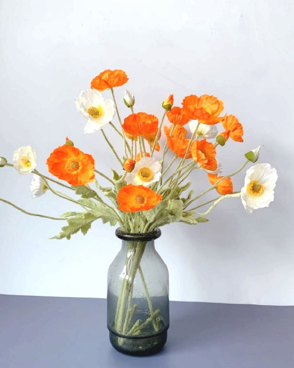 Orange and white poppies arranged together in a glass bottle