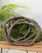 The coiled brown artificial rattan vine resting on a wooden table above a bed of moss