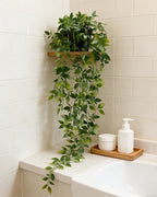 Artificial trailing vine on a small shelf above a bath, its stems falling past the tiles
