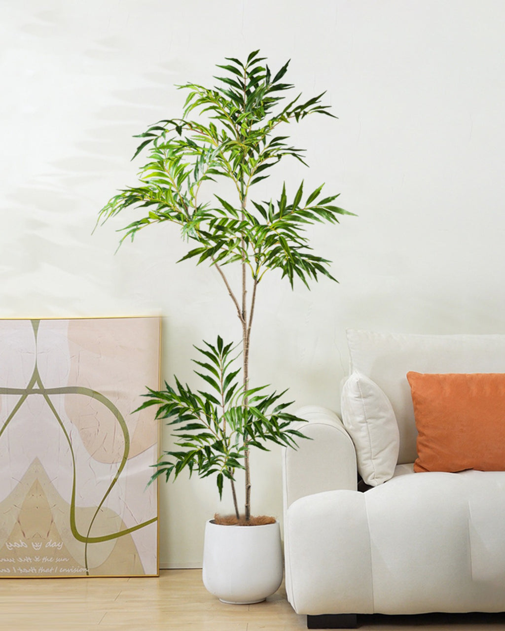The bamboo branch in a white pot beside a sofa and a framed print (pot not included)