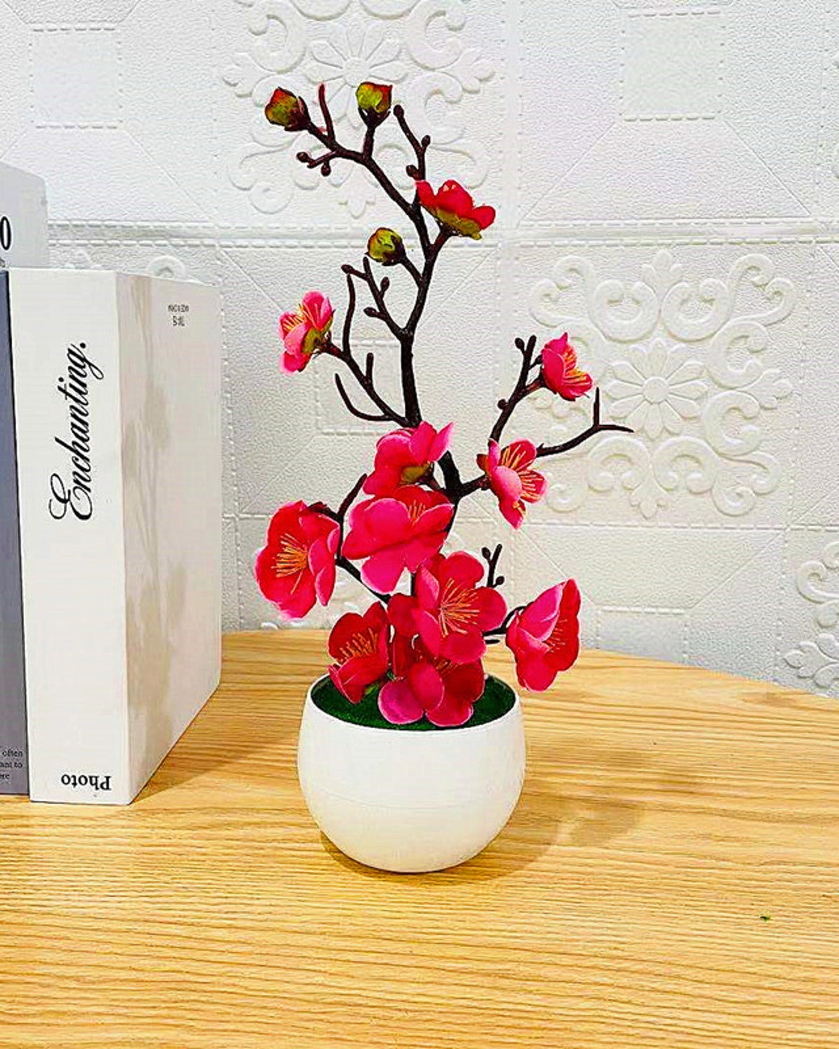 The rose red blossom bonsai on a wooden surface beside a stack of books
