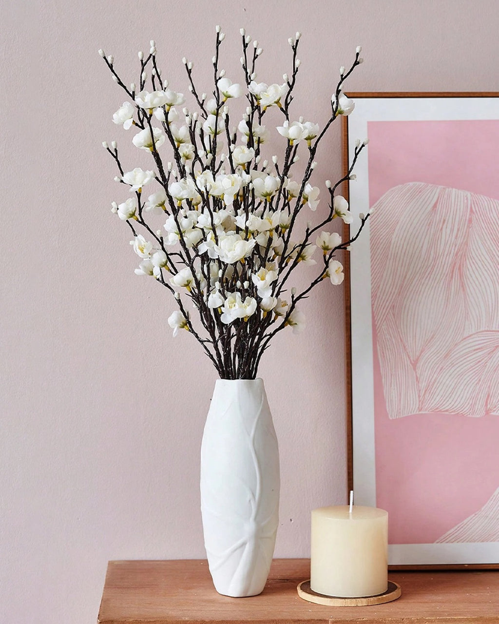 White plum blossom stems in a white vase beside a framed print and a candle (vase not included)