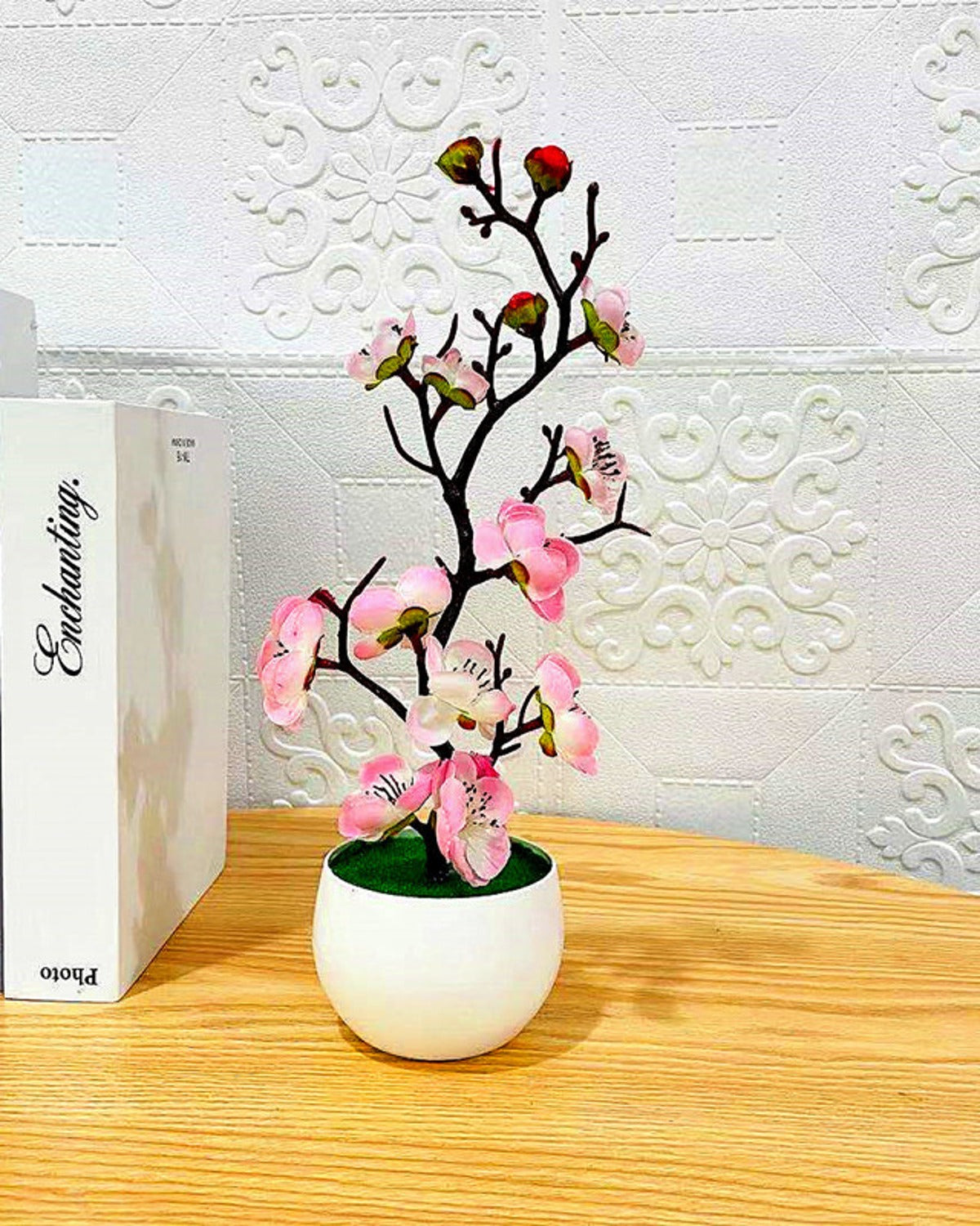 The pink blossom bonsai on a wooden surface beside a stack of books