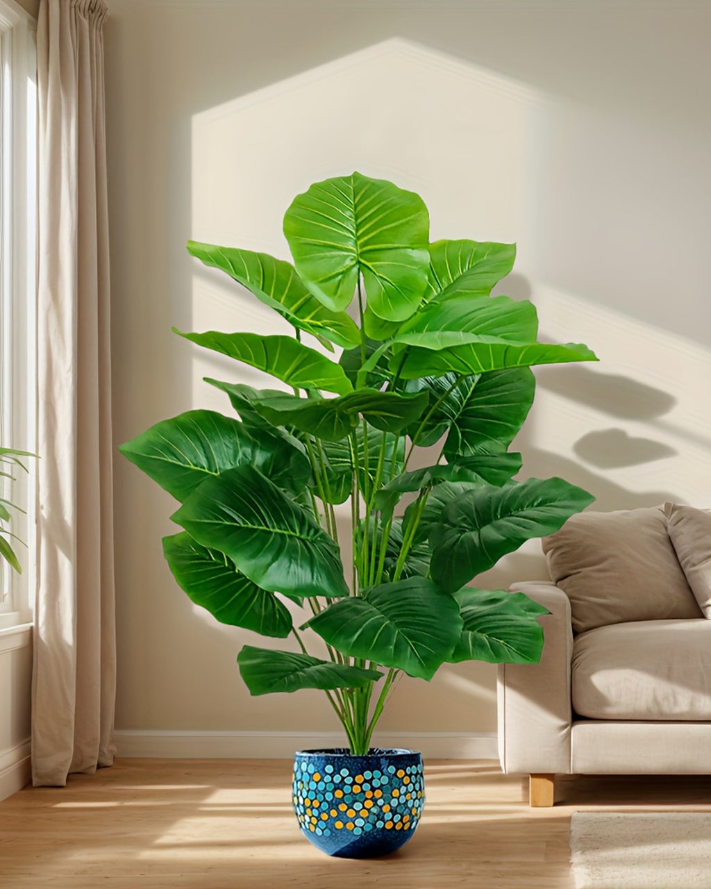 The elephant ear plant in a corner beside a pale sofa, its leaves catching the light (pot not included)