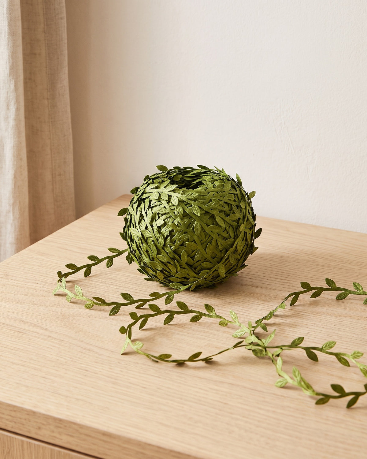 Coil of artificial leaf trim vine on a pale oak table