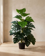 Artificial monstera plant on a pale oak floor against a plaster wall, shown in a plain pot for support, pot not included