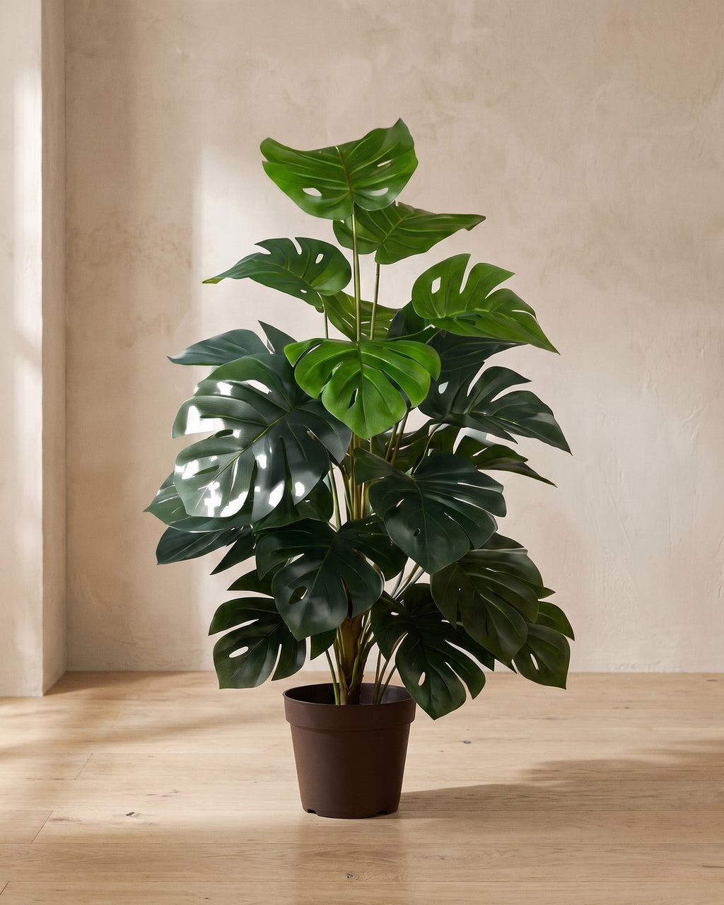Artificial monstera in a plain nursery pot in the corner of a room (pot not included)