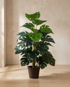 Artificial monstera in a plain nursery pot in the corner of a room (pot not included)