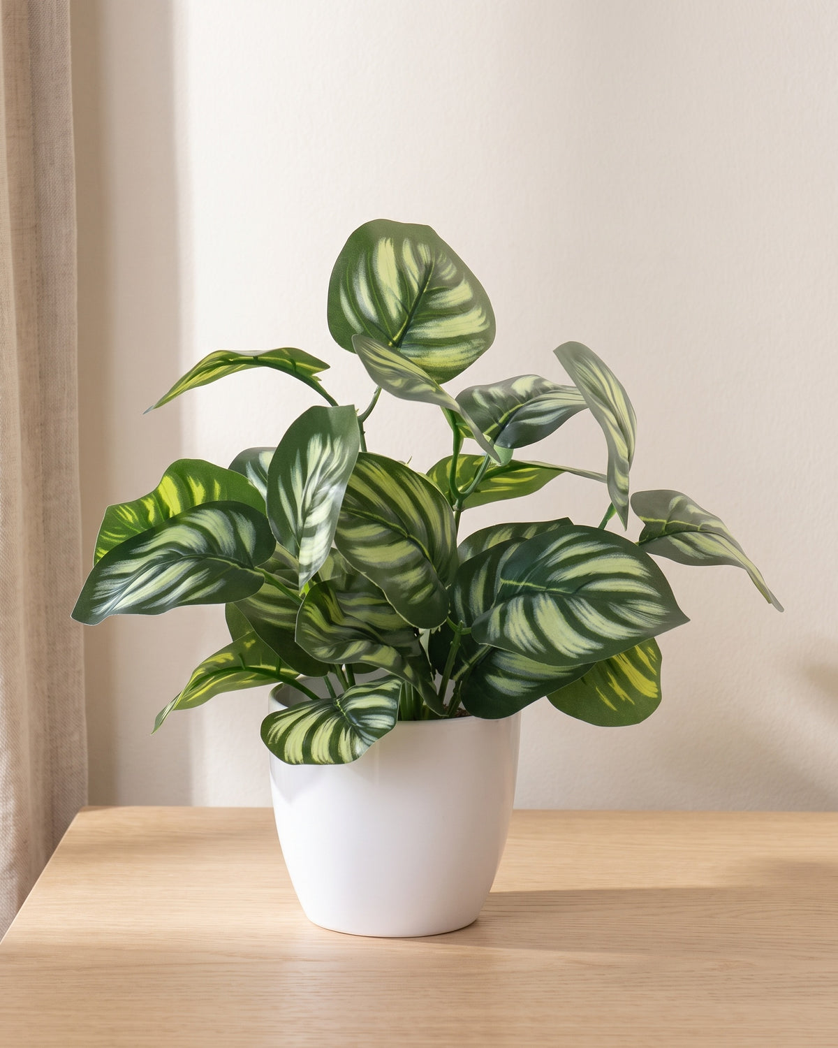 Small artificial potted foliage plant in a white ceramic pot on a pale oak tabletop
