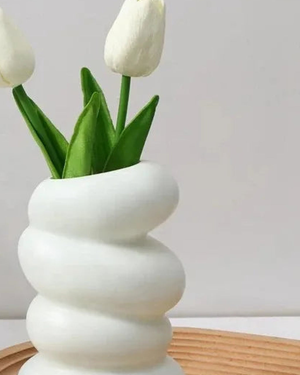A spiral bud vase holding tulips on a wooden tray; tulips and tray not included
