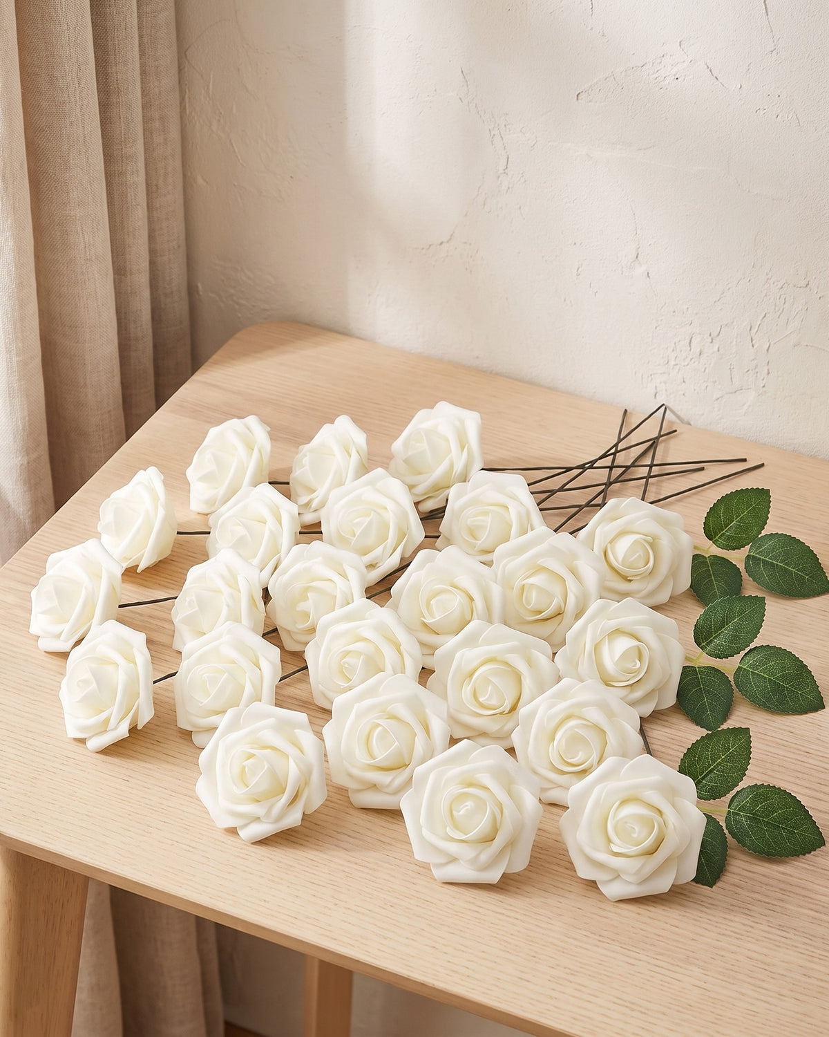 Twenty-five ivory foam rose heads on wire stems laid out on a pale oak table