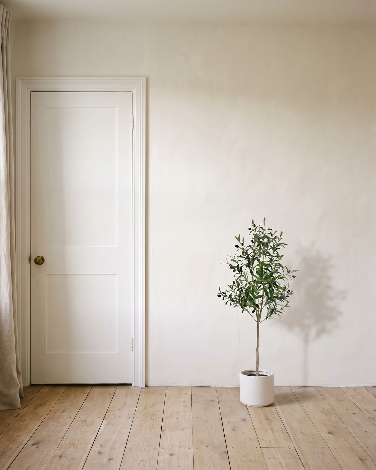 The 47 in artificial olive tree in a plain white pot, beside an 80 in door to show its height; planter not included