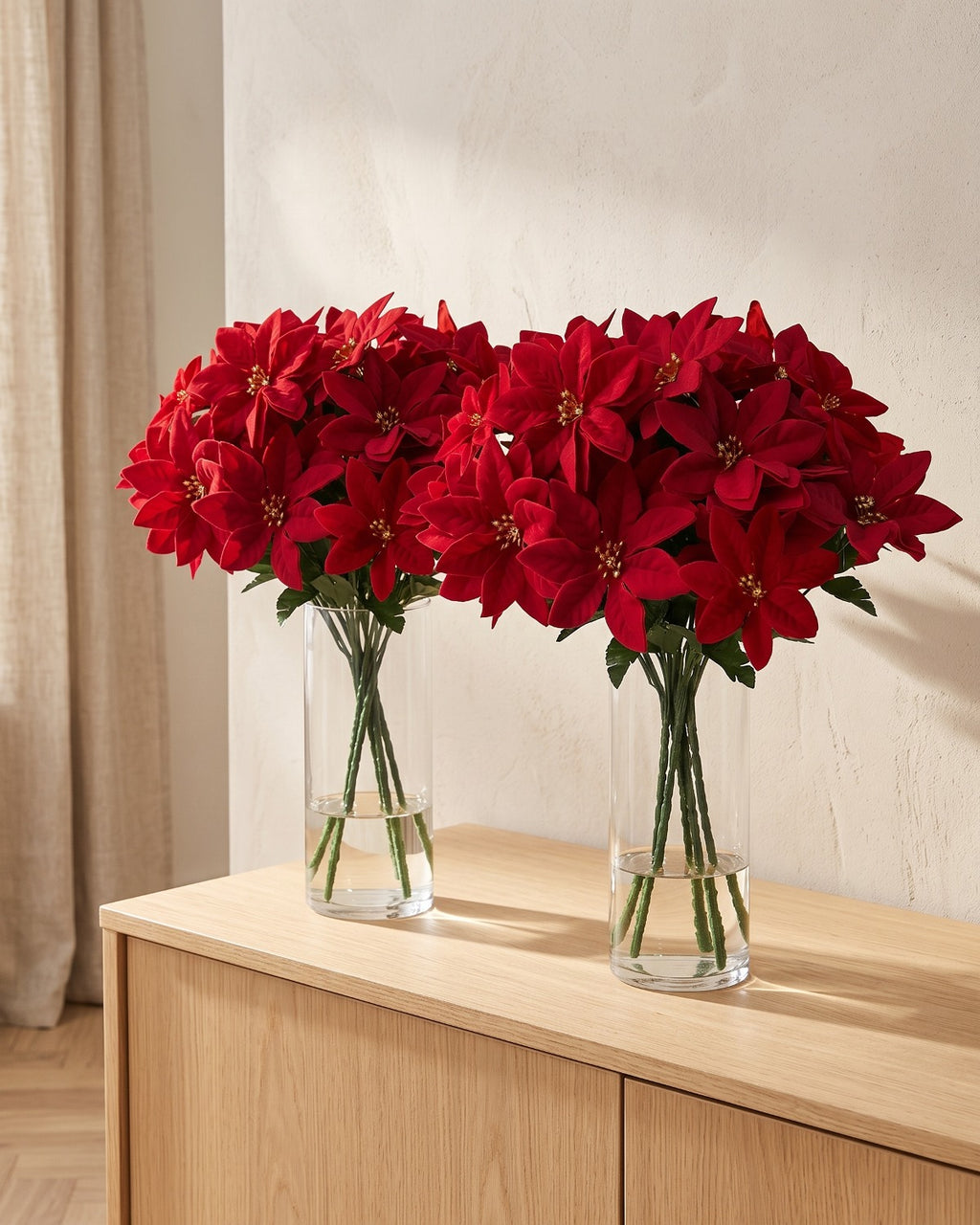 Red artificial poinsettia bouquets in two clear glass vases on a sideboard; vases not included