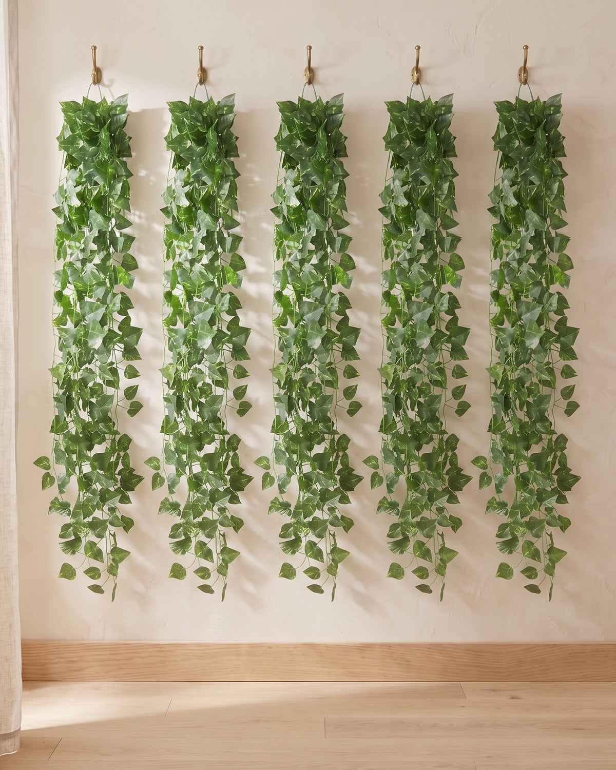 Five strands of the pointed leaf artificial ivy garland, 6.5 ft each, hanging side by side from five hooks on a plain wall: the 33 ft option