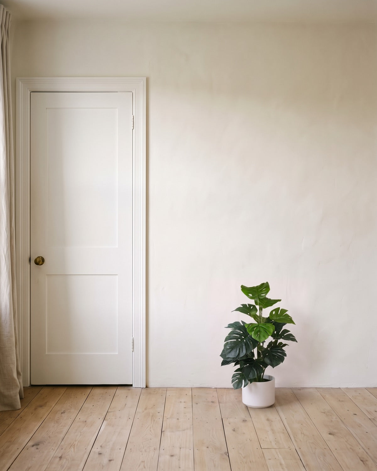 The 29.5 in artificial monstera plant with eighteen leaves, in a plain white pot beside an 80 in door to show its height; pot not included