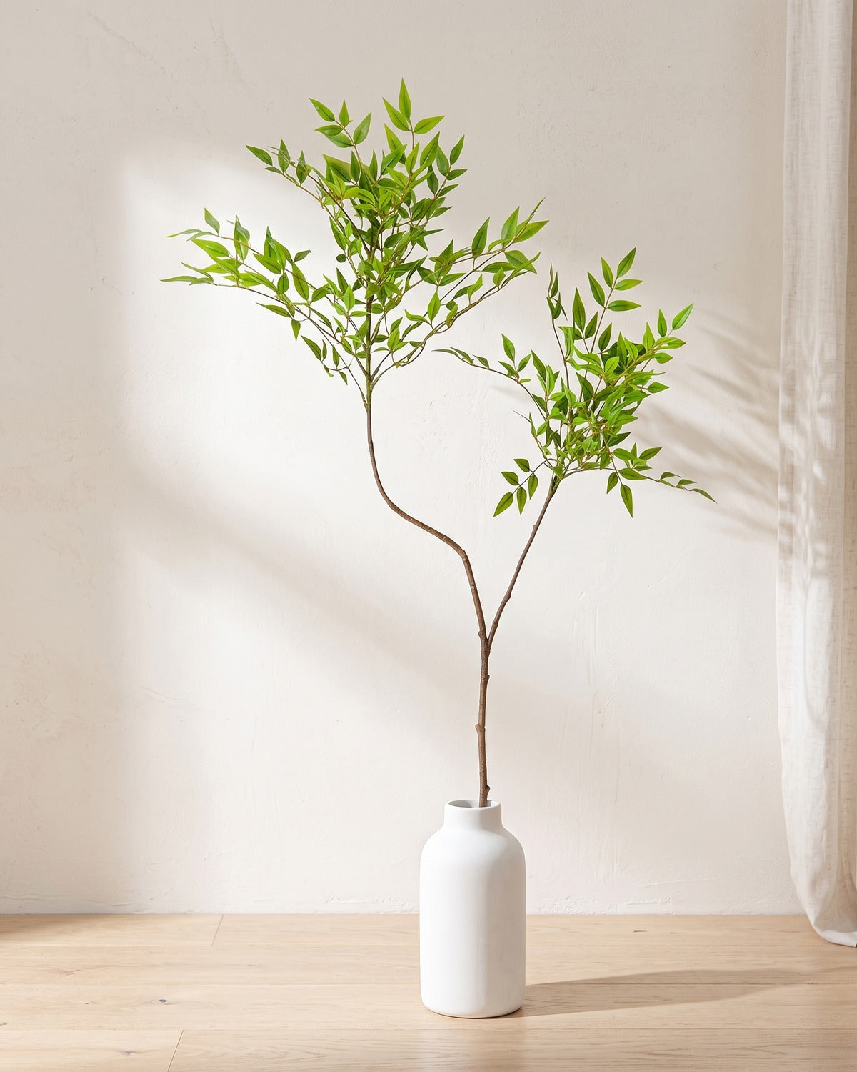 Fine leaf artificial tree branch, 2 stems, 43.3 in, standing in a plain white vase on a pale oak table; no vase is included