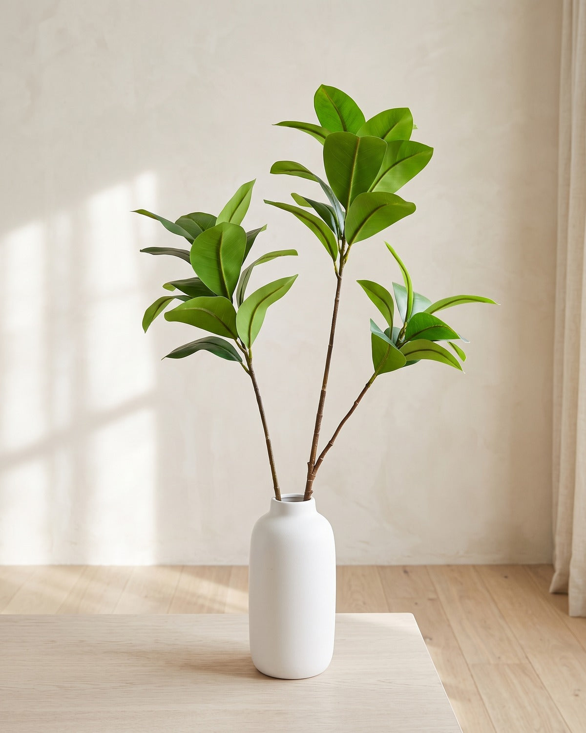 Glossy oval leaf artificial tree branch, set of 2, 41.3 and 33.9 in, standing in a plain white vase on a pale oak table; no vase is included