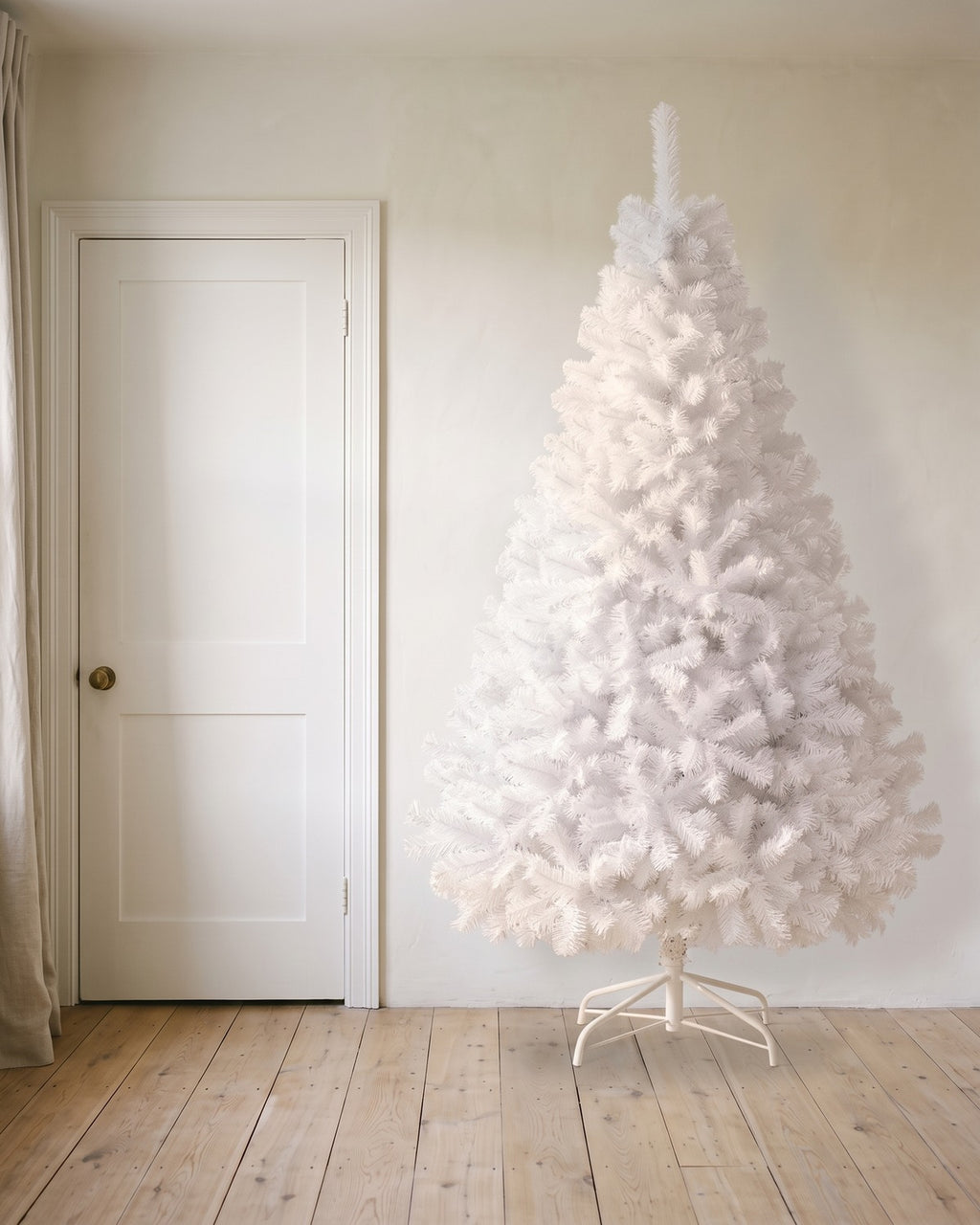 A white artificial Christmas tree at 8 ft on its folding stand, beside an 80 in door to show its height