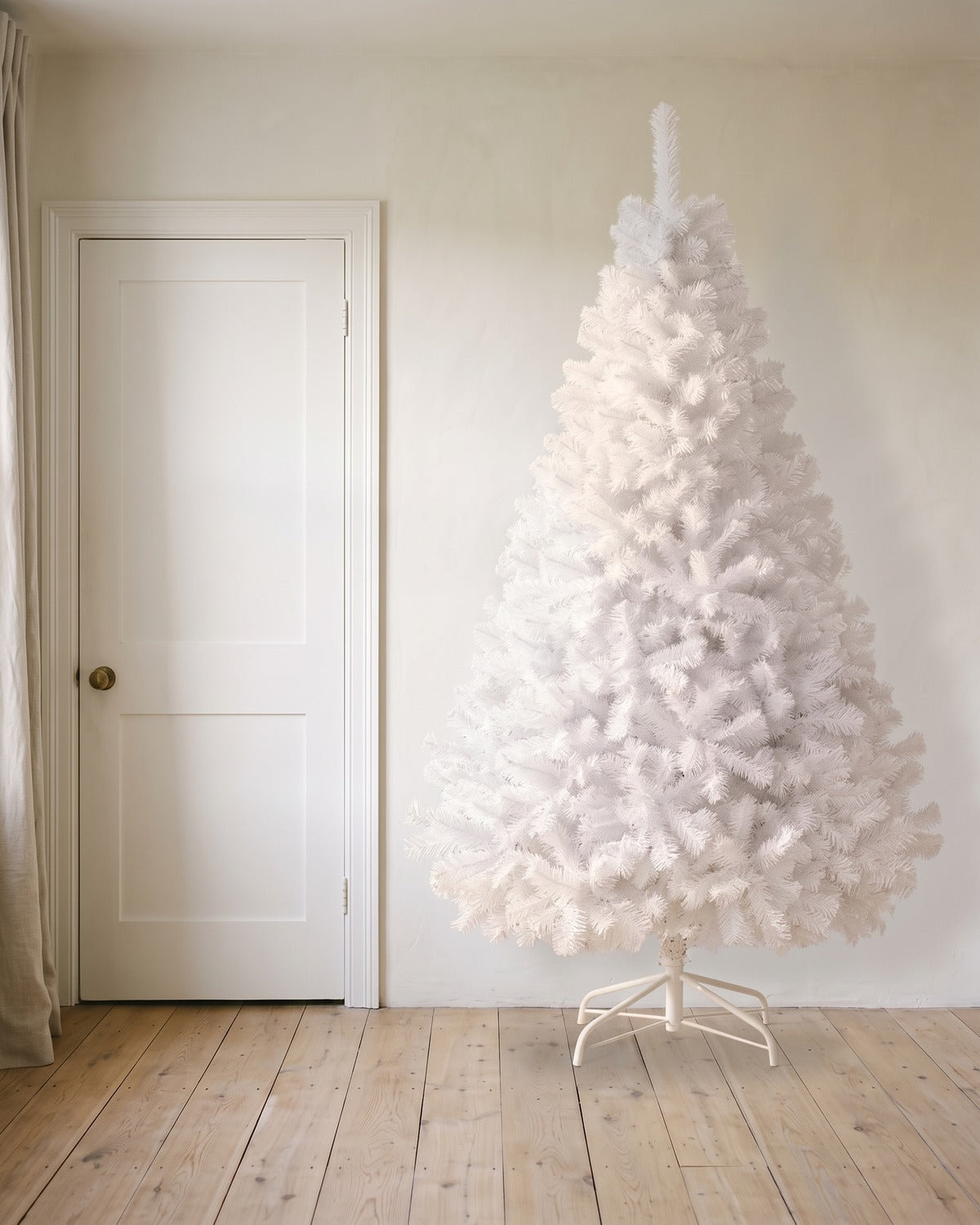 A white artificial Christmas tree at 8 ft on its folding stand, beside an 80 in door to show its height