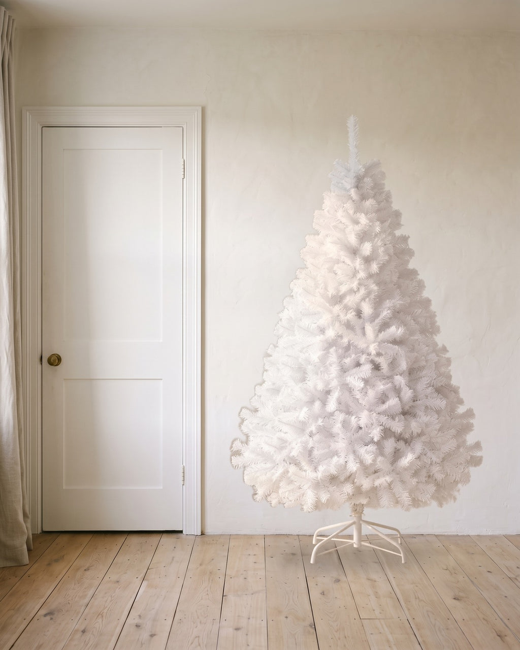 A white artificial Christmas tree at 7 ft on its folding stand, beside an 80 in door to show its height