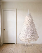A white artificial Christmas tree at 7 ft on its folding stand, beside an 80 in door to show its height