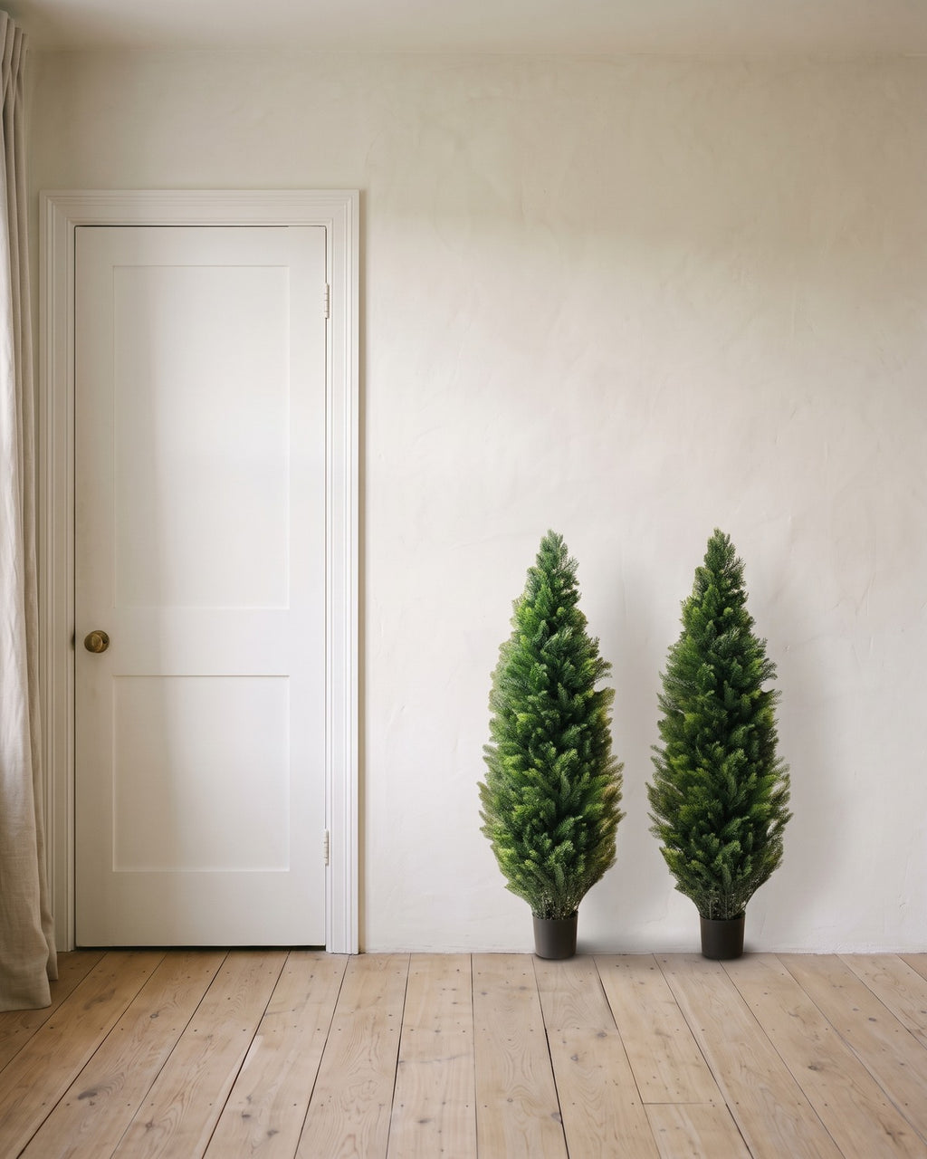 A pair of artificial cedar topiary trees at 48 in, in black nursery pots, beside an 80 in door to show their height