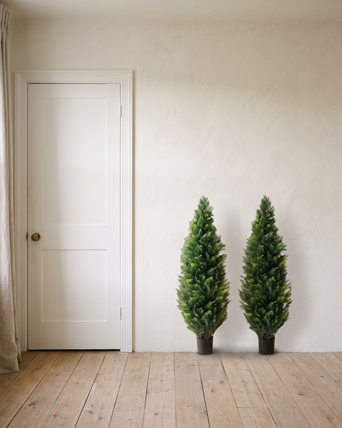 A pair of artificial cedar topiary trees at 48 in, in black nursery pots, beside an 80 in door to show their height