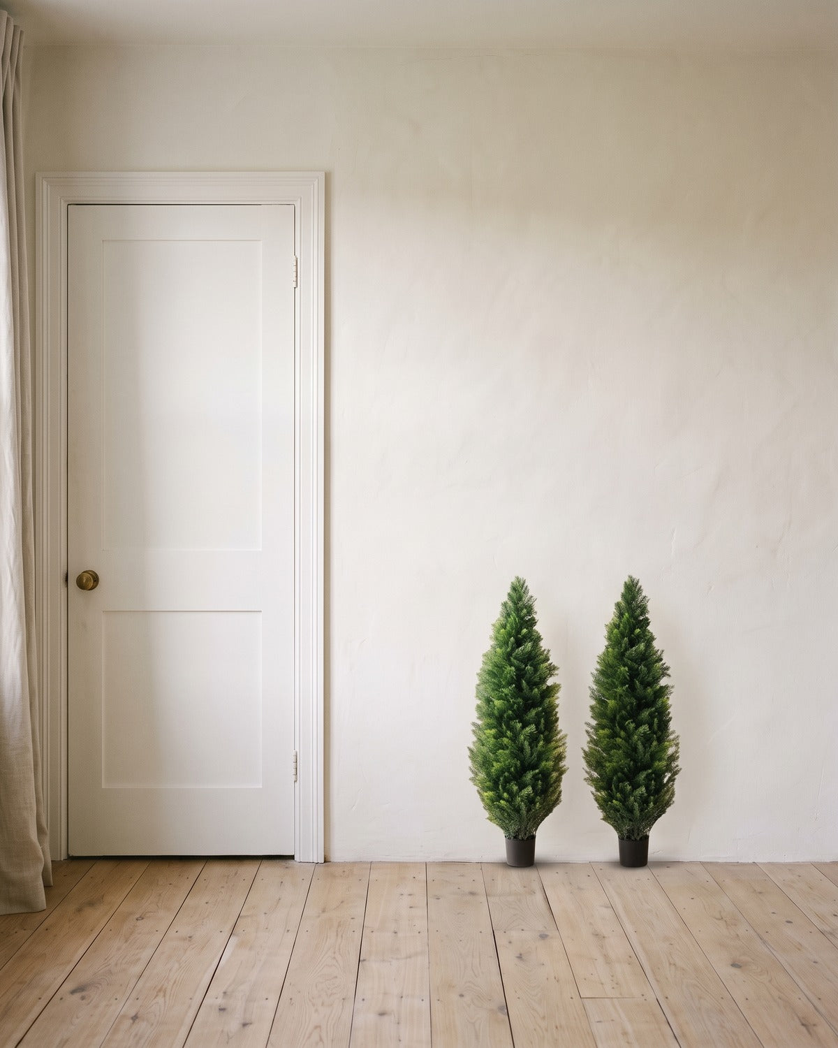 A pair of artificial cedar topiary trees at 36 in, in black nursery pots, beside an 80 in door to show their height