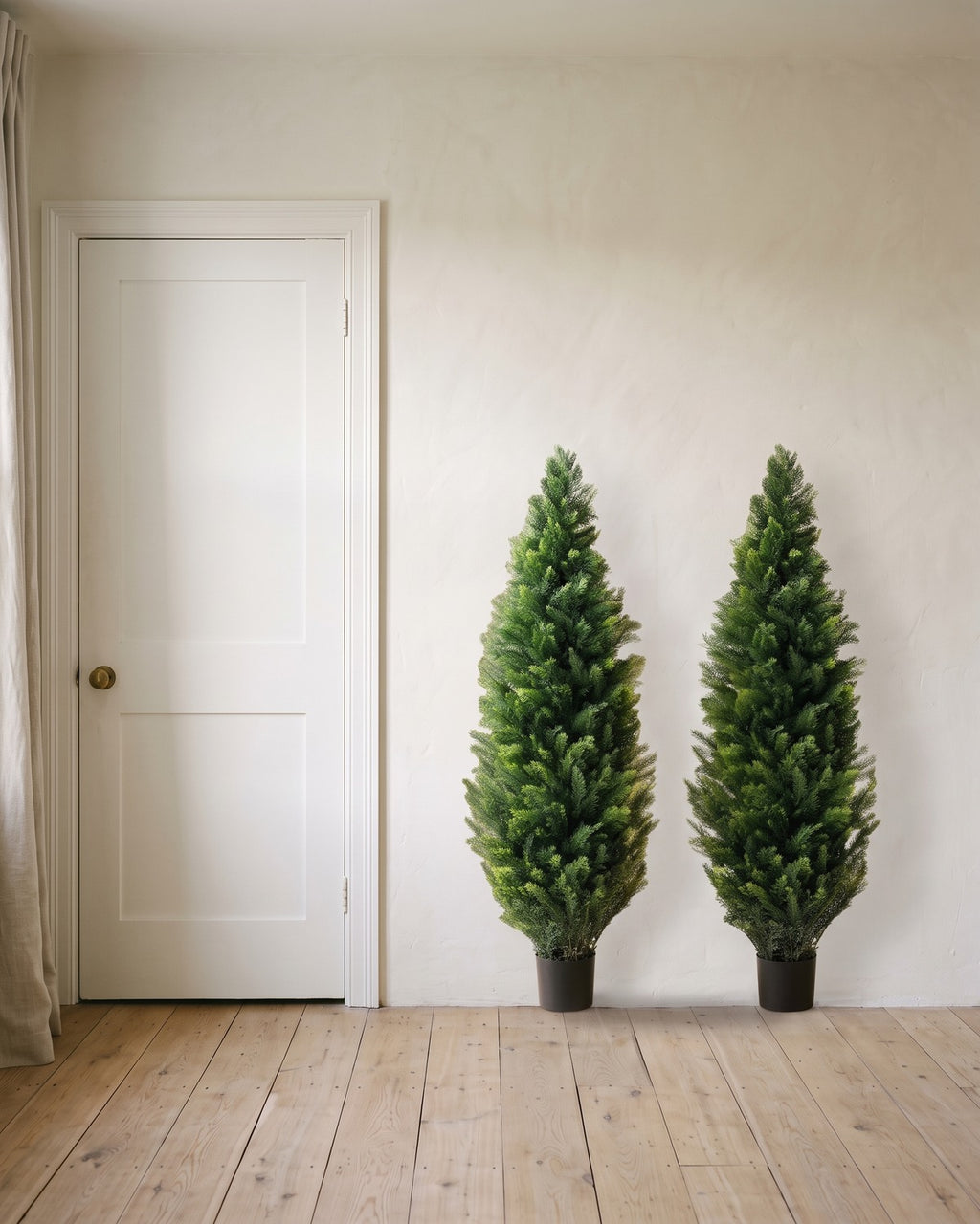 A pair of artificial cedar topiary trees at 60 in, in black nursery pots, beside an 80 in door to show their height