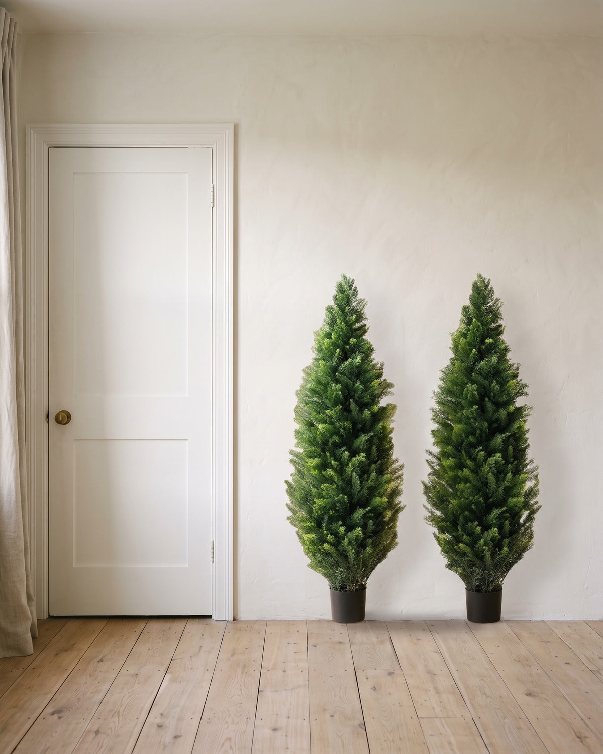 A pair of artificial cedar topiary trees at 60 in, in black nursery pots, beside an 80 in door to show their height