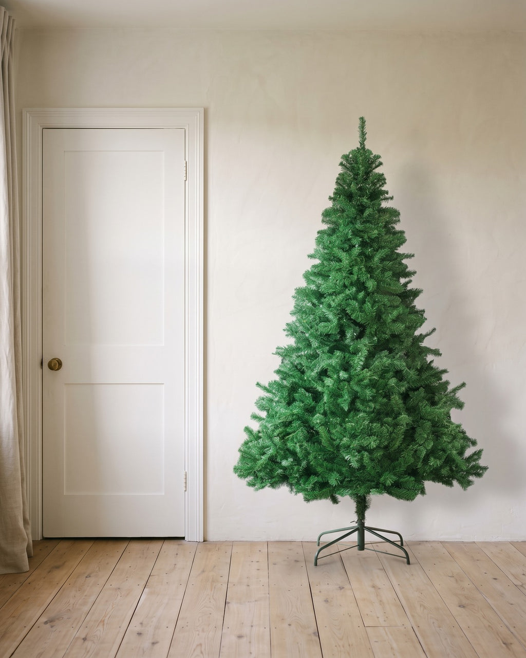 A green artificial spruce Christmas tree at 7 ft on its folding stand, beside an 80 in door to show its height