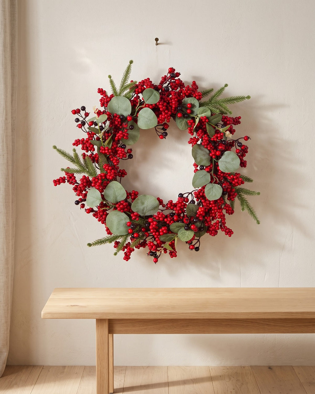 Berry and eucalyptus Christmas wreath hanging on a plaster wall above a bench