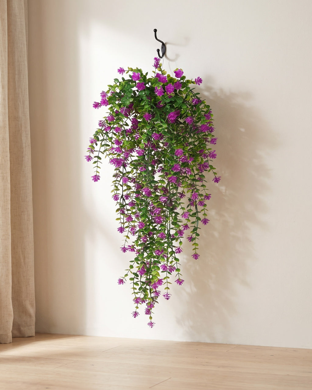 One artificial flowering hanging vine on a black iron hook against a warm plaster wall